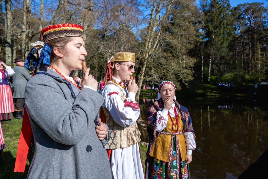 Palangos Jurginės. Trys tautiškai apsirengusios merginos groja skudučais prie Birutės parko tvenkinio.